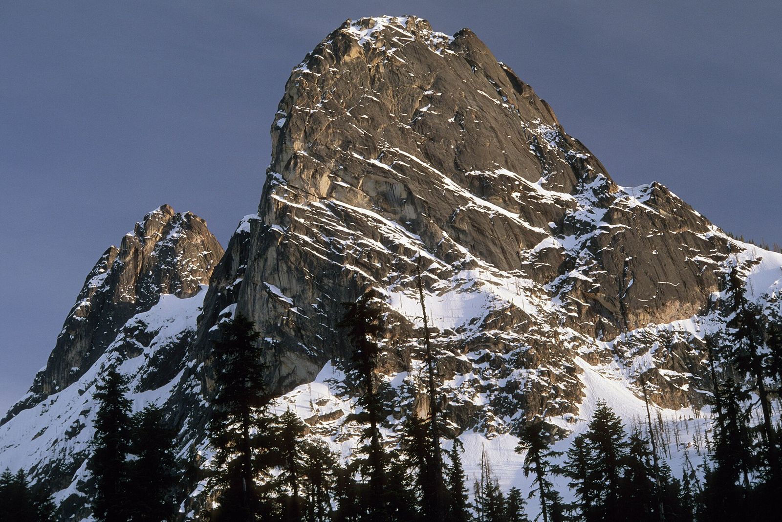 Granite face of Liberty Bell Mountain and Early Winters Spire with snow and evergreen trees in spring