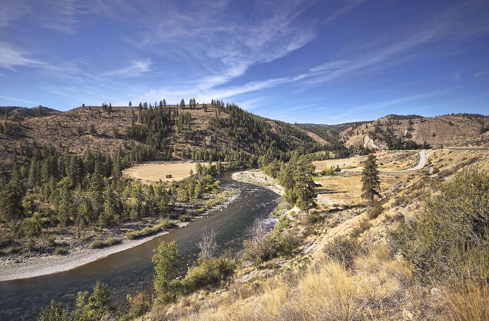 The Methow River curving through dry golden hills and pine forest under a blue sky