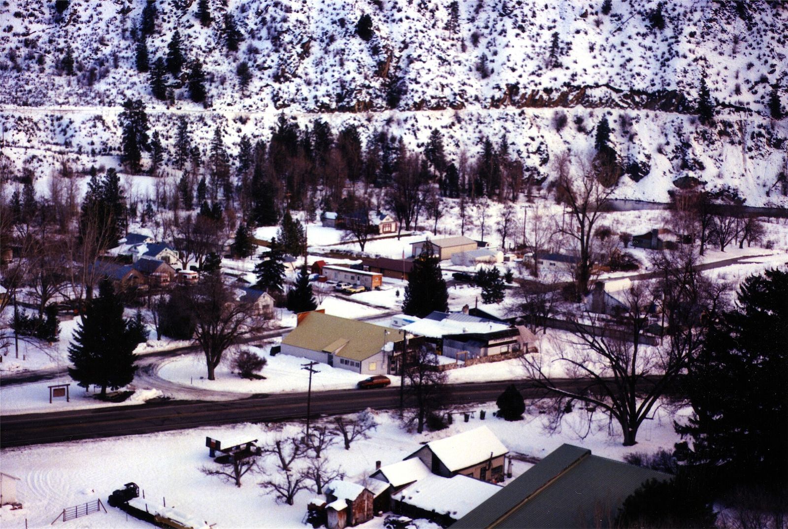 Small town with houses and trees blanketed in snow beneath snowy hillsides